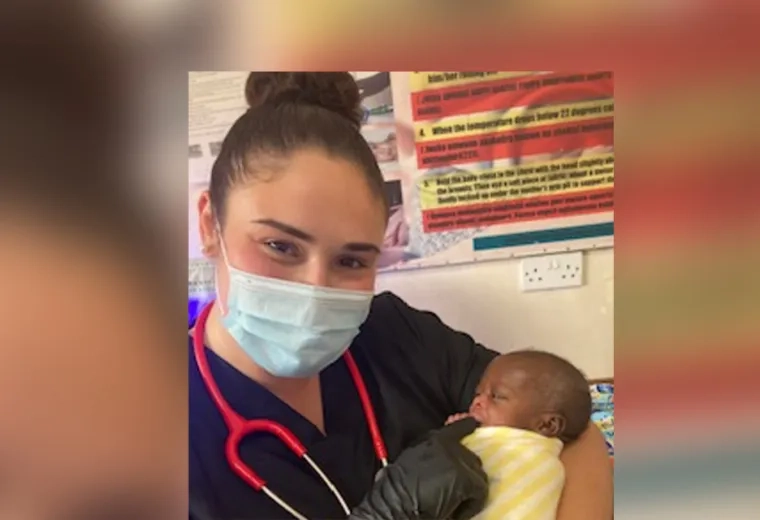 Leah wears a surgical mask and holds a tiny Black baby in her arms