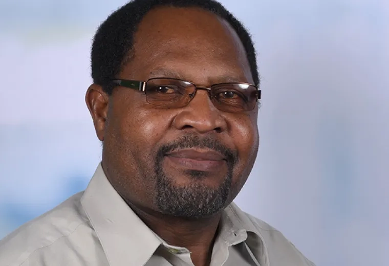 abraham wears a clay colored collared shirt and practical looking oval glasses