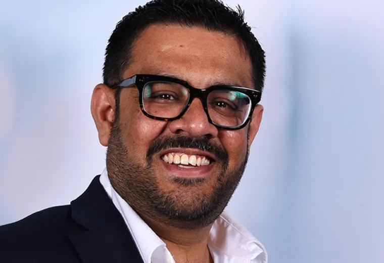 Dev wears a white collared shirt and black rimmed glasses