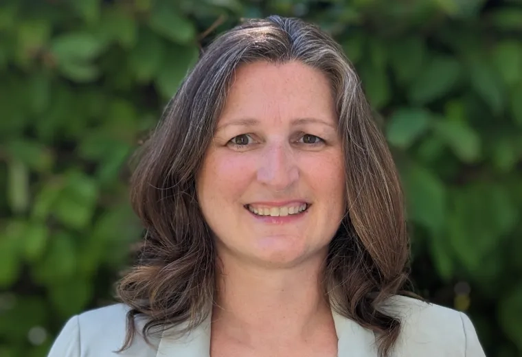 caitlin stands in front of a green bush and wears a seafoam colored blazer