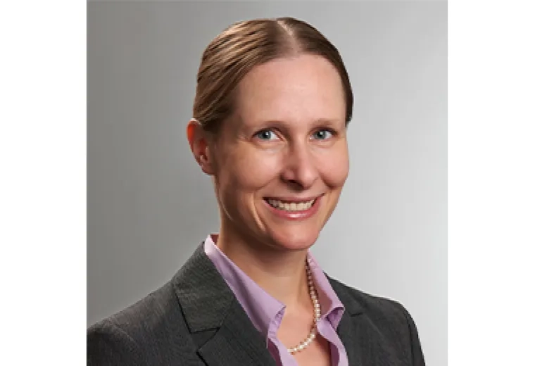 isabel has hair pulled back parted in the middle and wears a purple collared shirt under a grey blazer