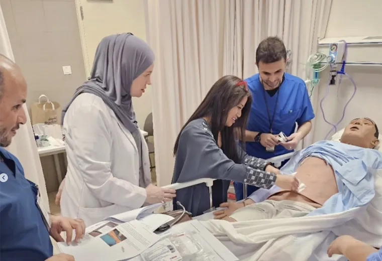two women and two men place a bandage on a manikin in a bed