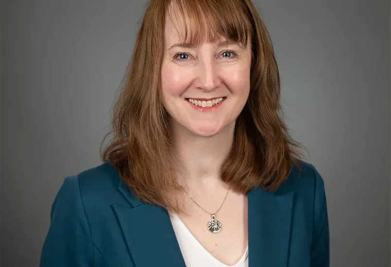 kathy wears a dark teal jacket and has strawberry blonde shoulder length hair