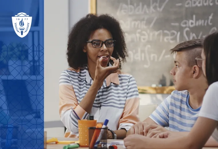 a woman in a classroom holds her hand to her mouth to show how to form a word to two younger students