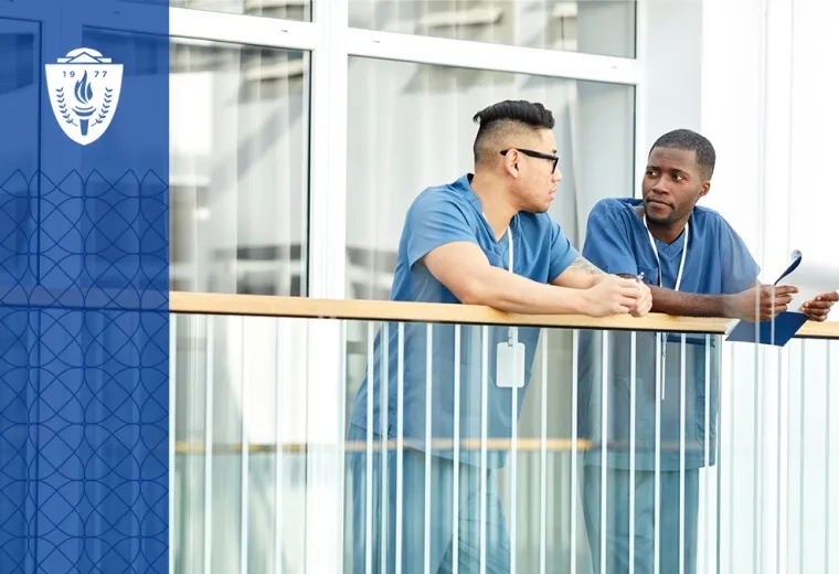 two men in scrubs lean on a hospital railing and converse with each other