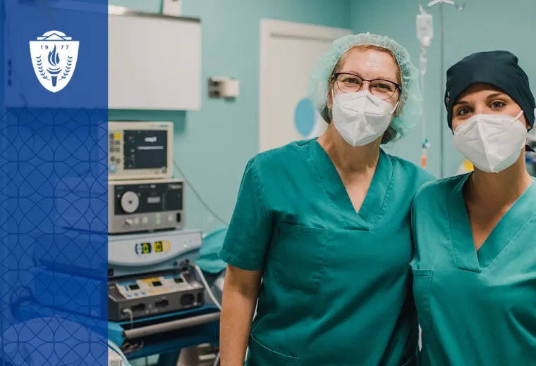 two women with masks and green scrubs stand arm and arm