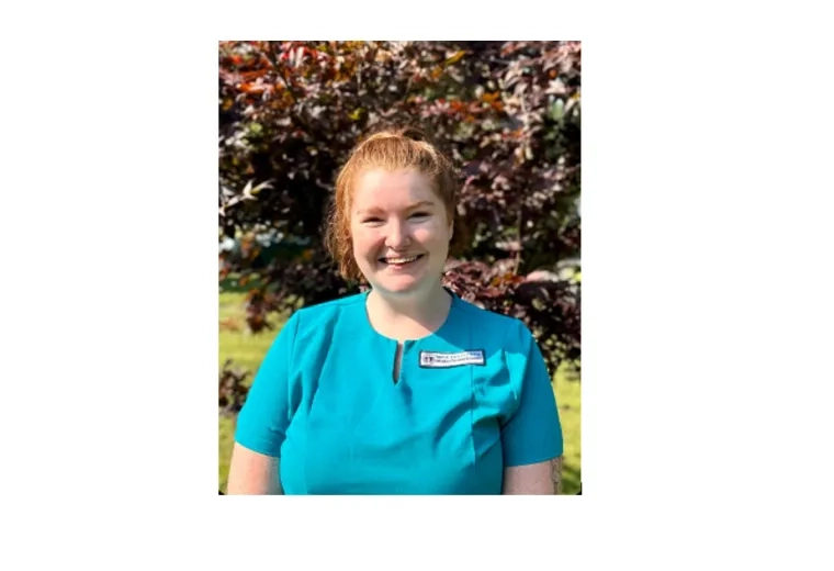 woman stands and smiles while wearing scrubs
