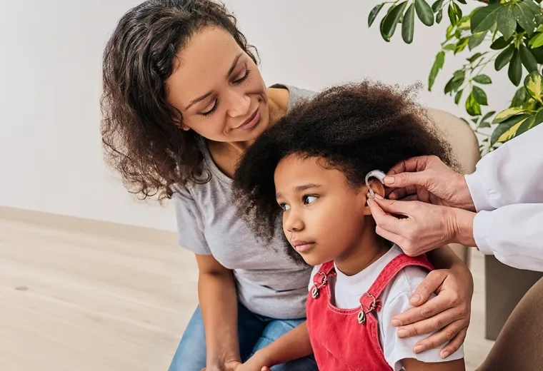 small girl is fitted for a hearing aid while her mom has her arm around her