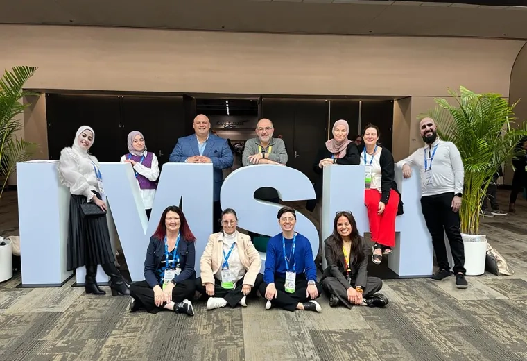 group of people stand in front of and within large letters spelling IMSH