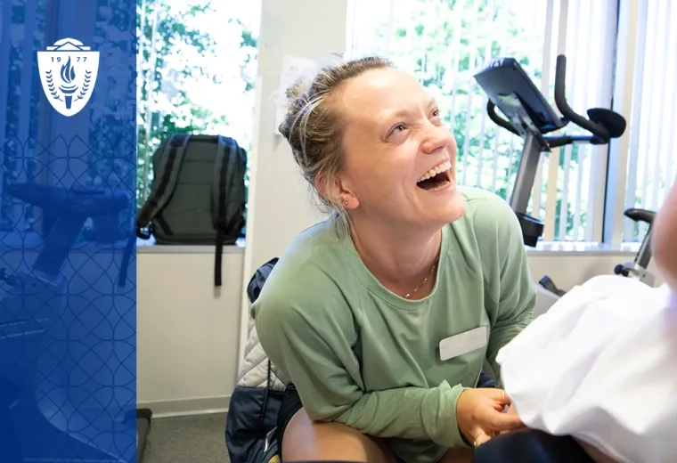 woman smiles broadly up at a person on a treatment table while she helps them move their leg