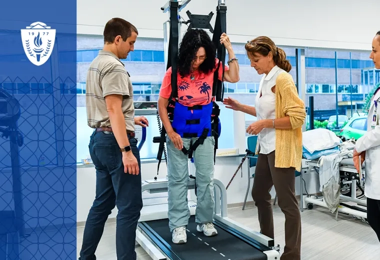 three people stand around a woman in a harness suspended over a treadmill in a gym