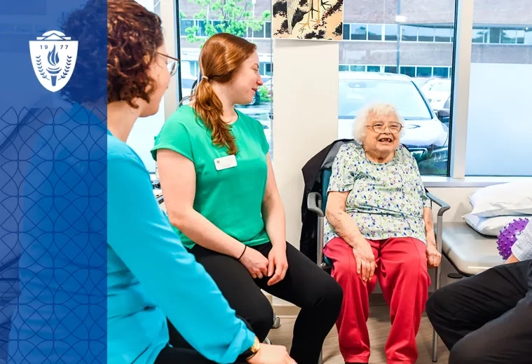 group of people sit around an older woman in a PT gym