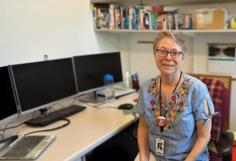 antonia has a brightly flower patterned blouse on and sits in an office chair