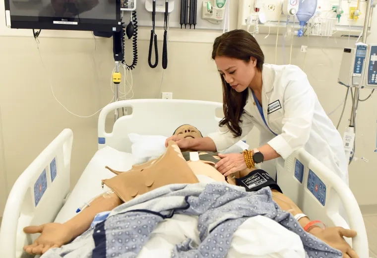 a woman in a lab coat leans over a manikin in a hospital bed