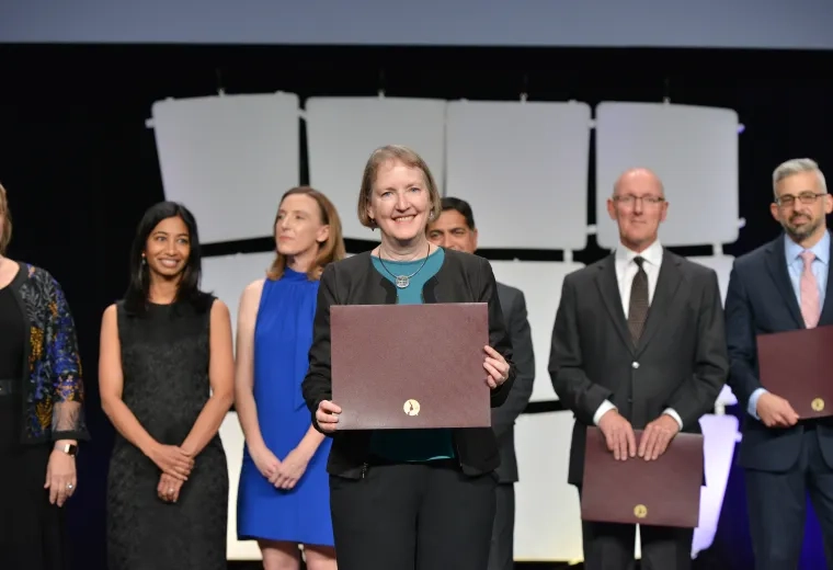 A woman standing on a stage holding an award with a line of people behind her