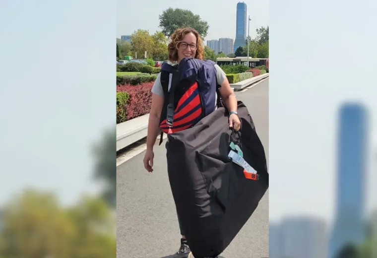 woman stands on a paved path with buildings and flowers in the background