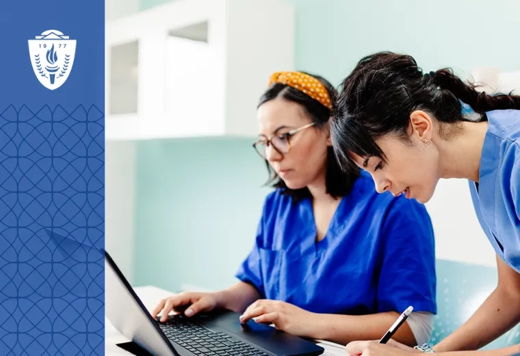 two women in scrubs work at a table with a laptop and pencil