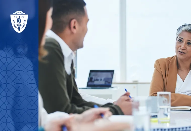 a woman with short grey hair sits at a conference table and talks to people in collared shirts