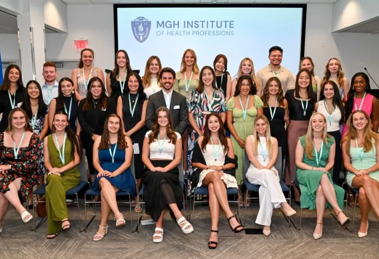 A group stands in three rows in front of a backdrop that says MGH Institute
