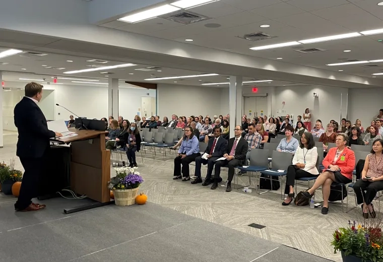 a large room with people seated listening to a man at a podium