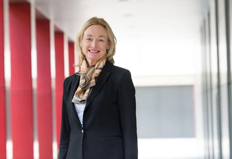 Debra Nestel has shoulder-length blonde hair and is wearing a black blazer and patterned scarf