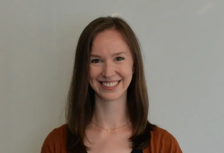 Eileen Gillan has medium brown hair and is wearing a black v-neck dress, and a orange cardigan