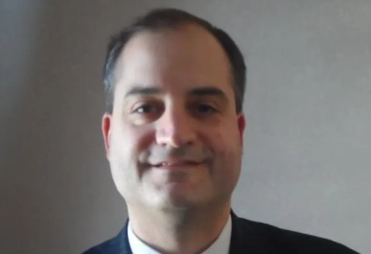 Gregory Hamann in a dark suit and white dress shirt with a striped tie.