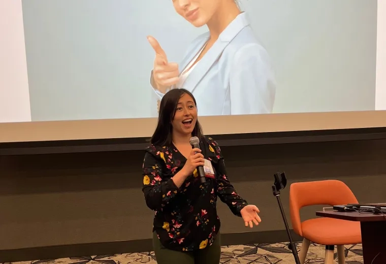 A woman stands in front of a screen holding a microphone