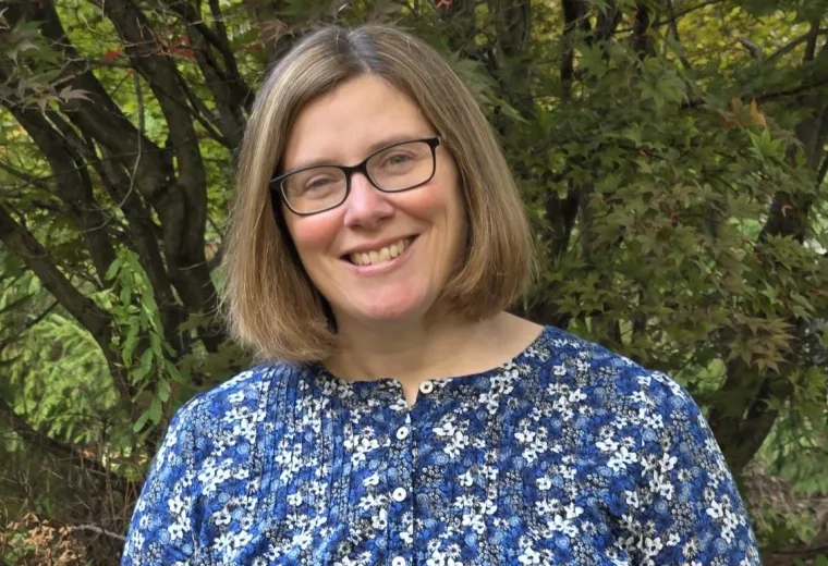 Susan Arruda has a short brown bob, glasses, and is wearing a blue floral shirt