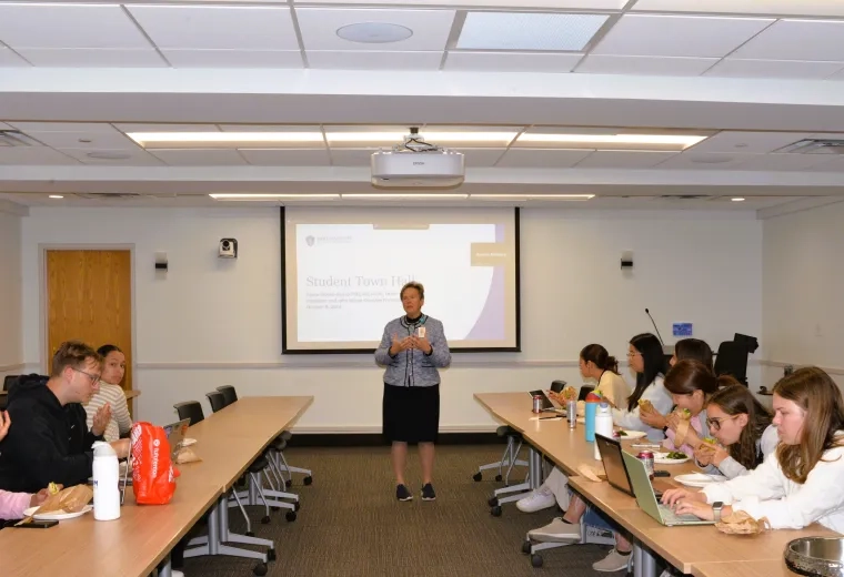 Woman standing in front of tables and students eating lunch 
