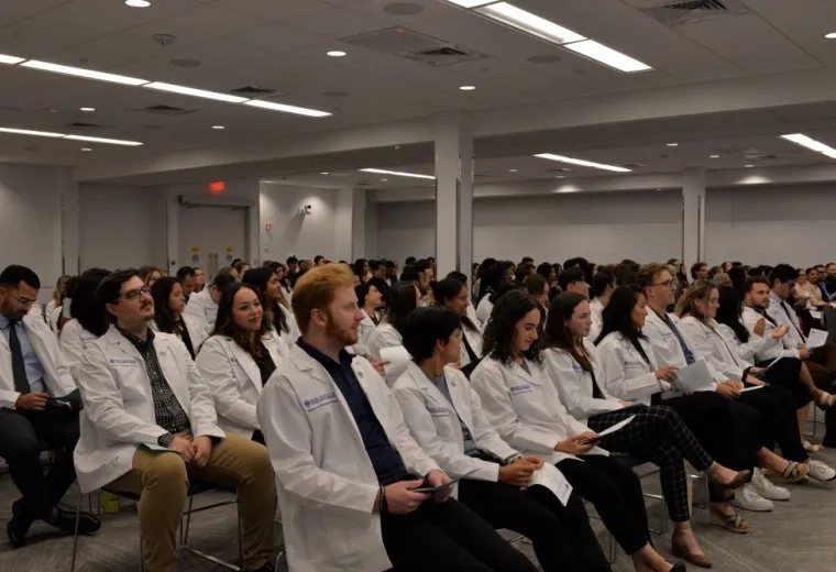 People wearing white physician coats sit in an audience