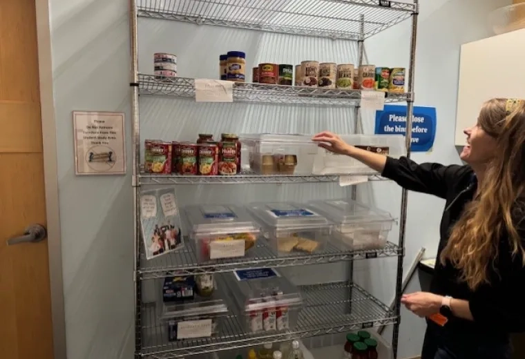 A woman stands in front of metal shelves with cans and boxes of food
