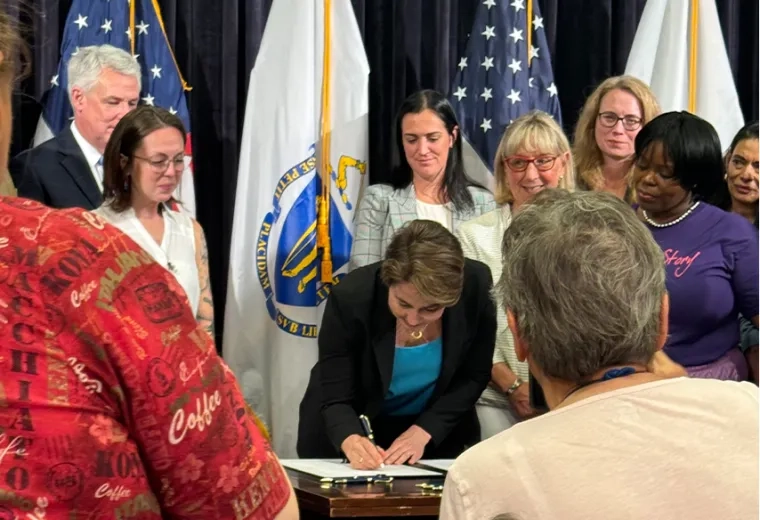 woman signs paper at desk with people all around