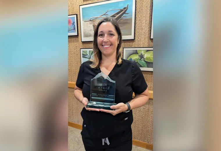 A woman holds an acrylic award with the words NBCOT Impact Award engraved on it