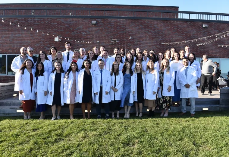 A group of people wearing white medical coats stand in three lines for a photo