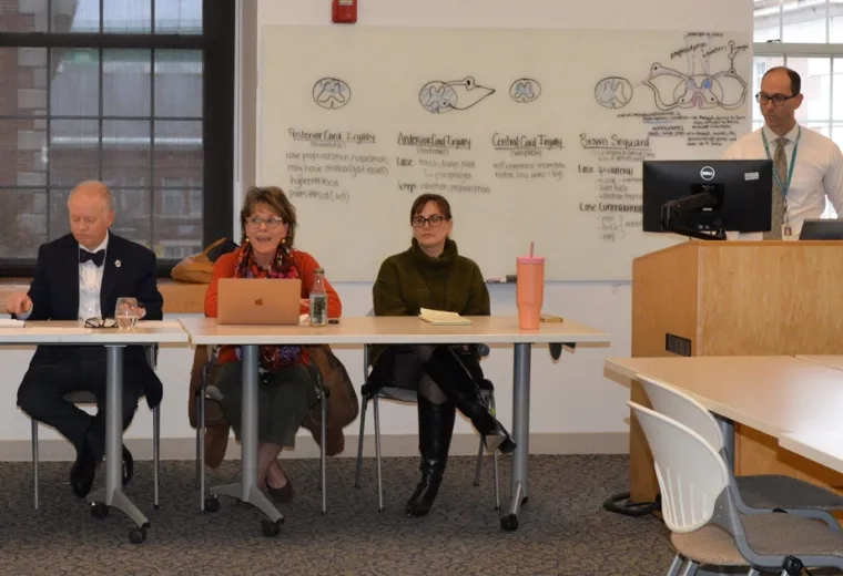 four people sit behind a table while a fifth person is at a podium with a computer