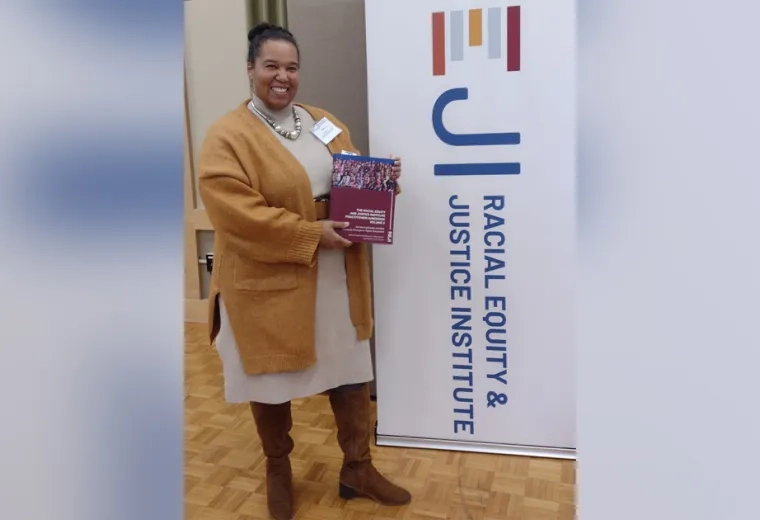 A woman stands in front of a sign holding a book