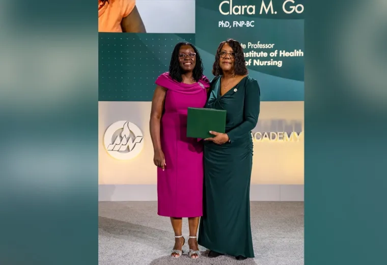 Two women pose holding a certificate in front of a screen