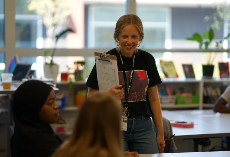 A professional in the MGH IHP Literacy and Language Certificate Program poses confidently in a modern academic setting. The program prepares educators for leadership roles in literacy education, emphasizing teaching reading and writing skills, and literacy leadership training. 