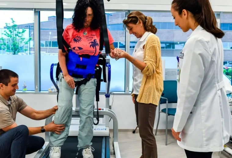 a woman in a harness walks on a treadmill surrounded by caregivers