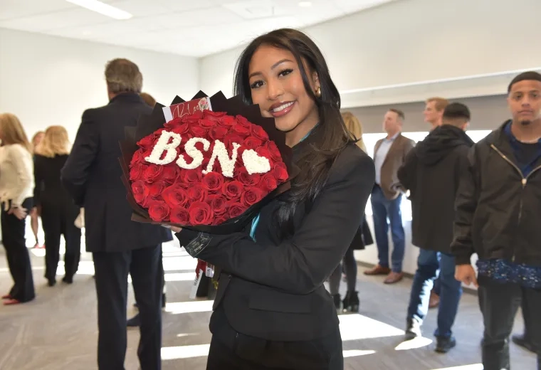 a woman holds a bouquet of red flowers with white flowers interspersed spelling BSN