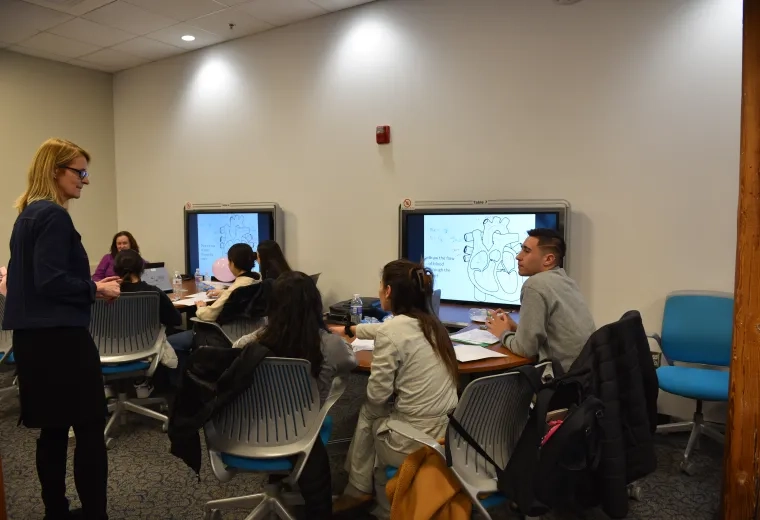 A woman who is standing faces a group of students sitting at a table