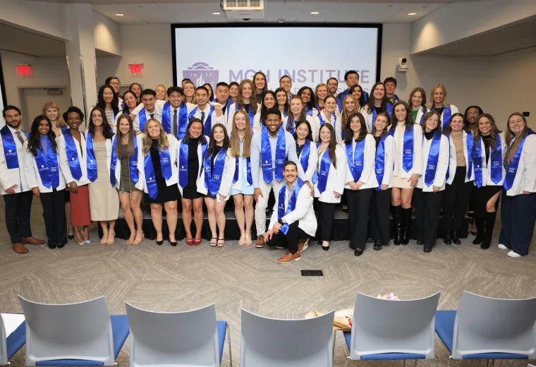 A large group poses for a photo wearing white coats and blue sashes around their necks