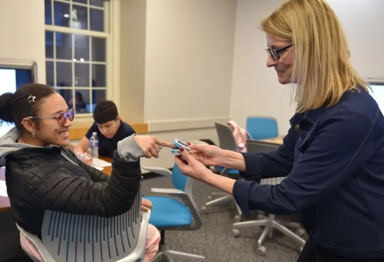 A woman places a device on the finger of a woman who is sitting down