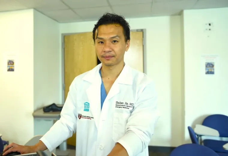 Doctor in lab coat looking into camera; coat has name and hosital affiliation 