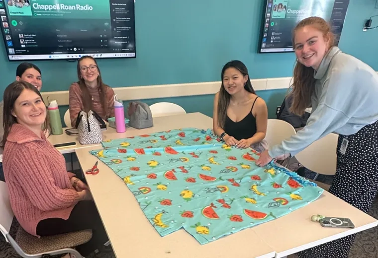 Students around table making fleece blanket 