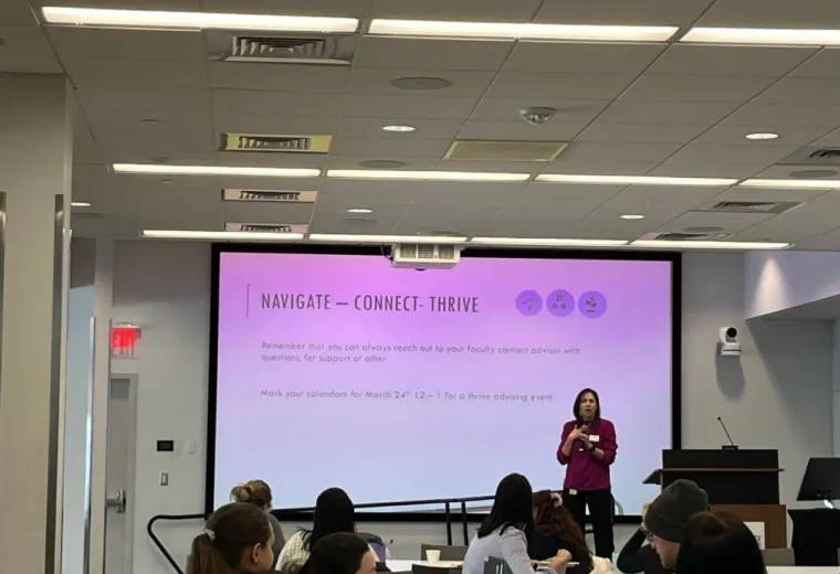 A woman stands on stage in front of a screen while people at tables sit in front of her. 