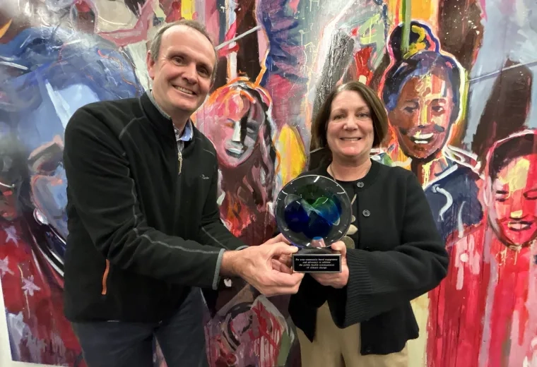 A man presents an award to a woman in front of a colorful mural on the wall