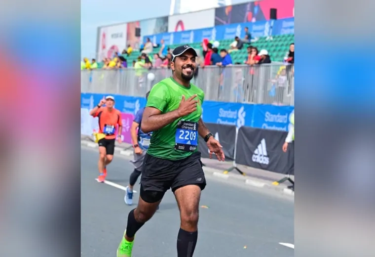 A man running wearing a green running top and a bib number