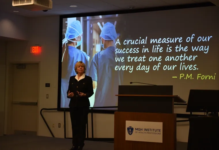 A woman stands in front of a screen with a quote